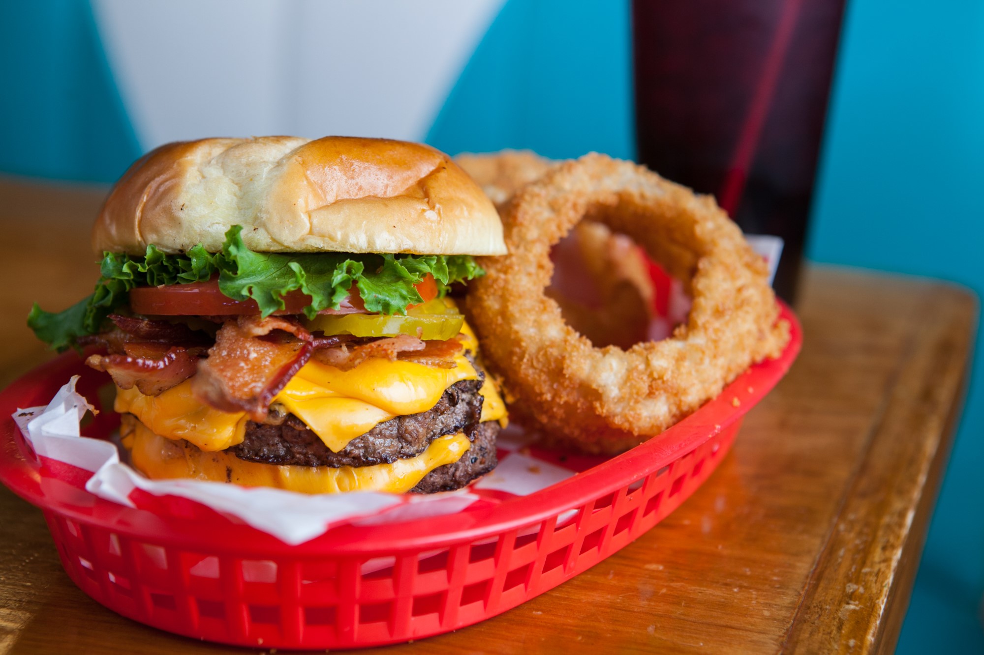 A cheeseburger with onion rings in a red basket